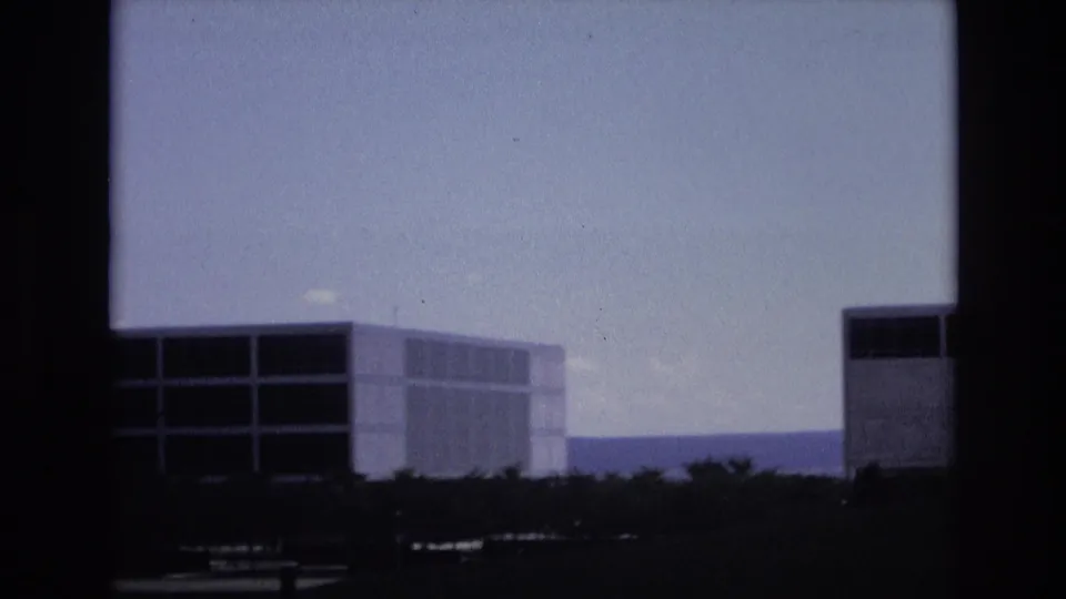 1973 Colorado Springs frame with a low, wide modernist building, horizontal window strips, trees at ground level, distant hills, and visible 8mm frame borders.