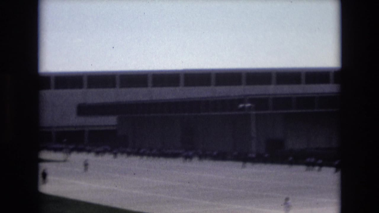 1973 Colorado Springs home-movie frame showing distant people crossing a wide paved plaza before a modern building with long window bands.