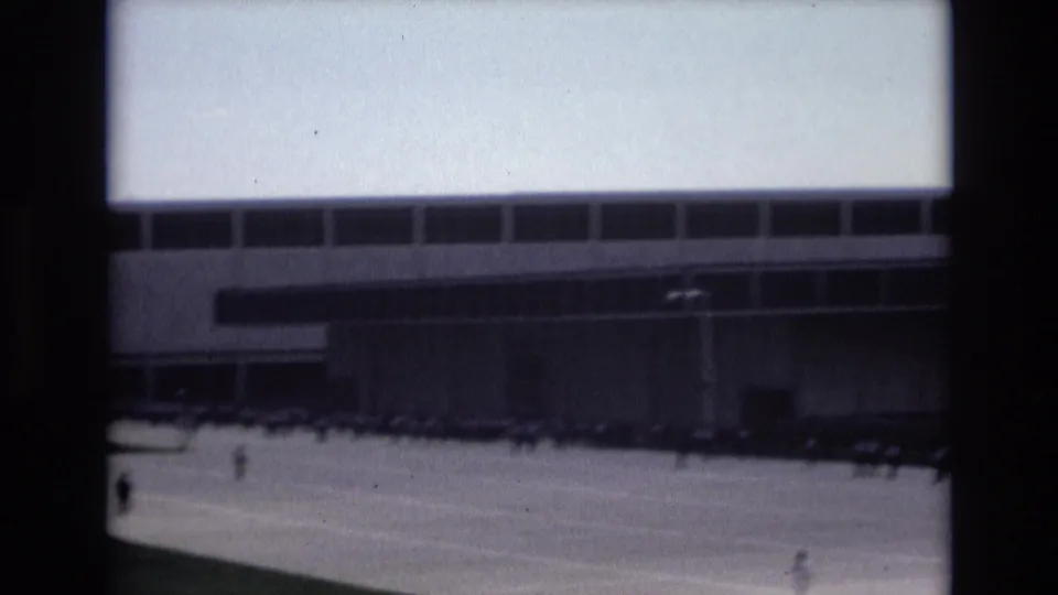 1973 Colorado Springs home-movie frame showing distant people crossing a wide paved plaza before a modern building with long window bands.
