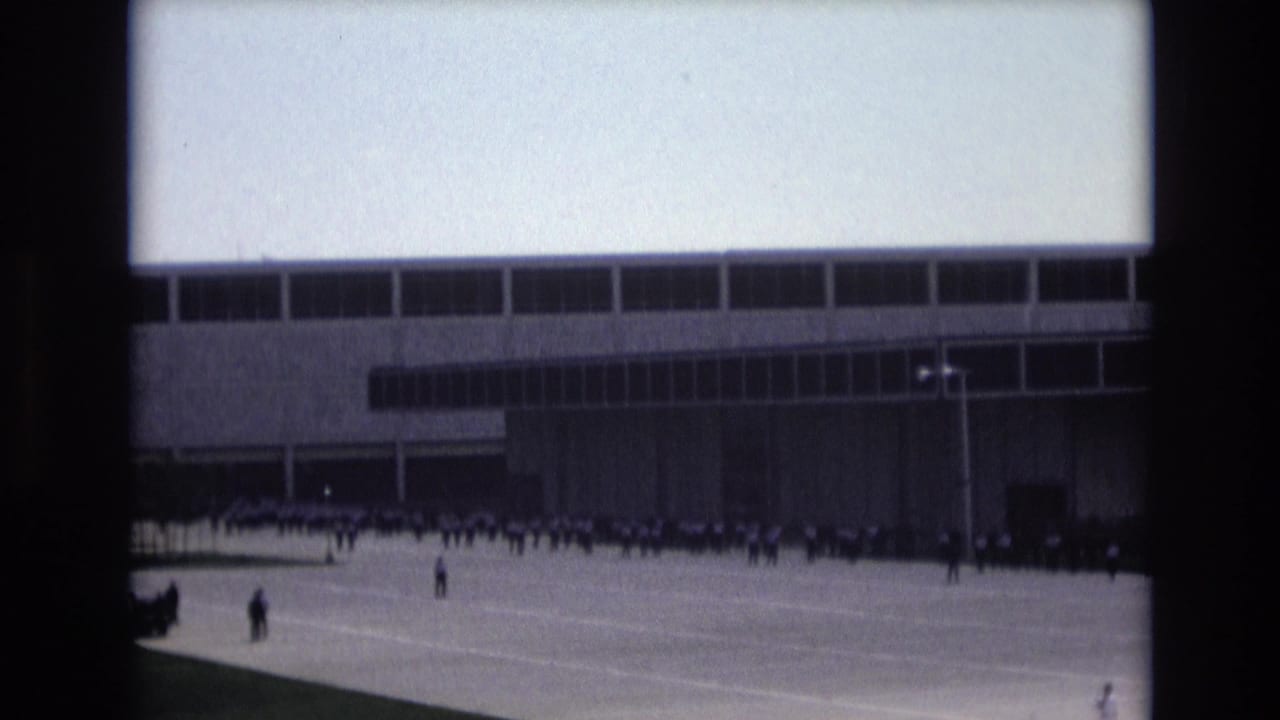 Distant group of people in Colorado Springs appears to move or assemble in formation outside a modernist building in 1973 archival 8mm footage.