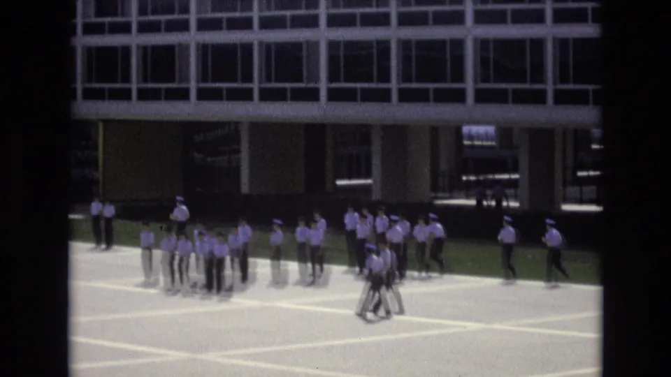 Uniformed personnel gather and move in formation on a paved area outside a large grid-windowed building, consistent with the supplied 1973 Colorado Springs military drill metadata.