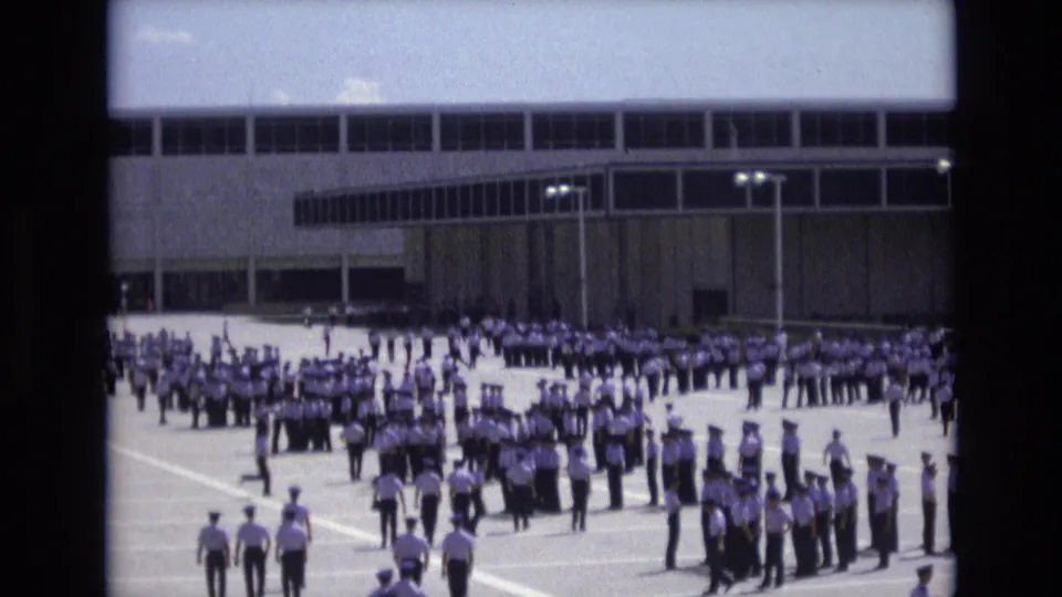A wider view shows large groups of uniformed cadets arranged across the courtyard near a modern institutional building in the 1973 Colorado Springs home-movie footage.
