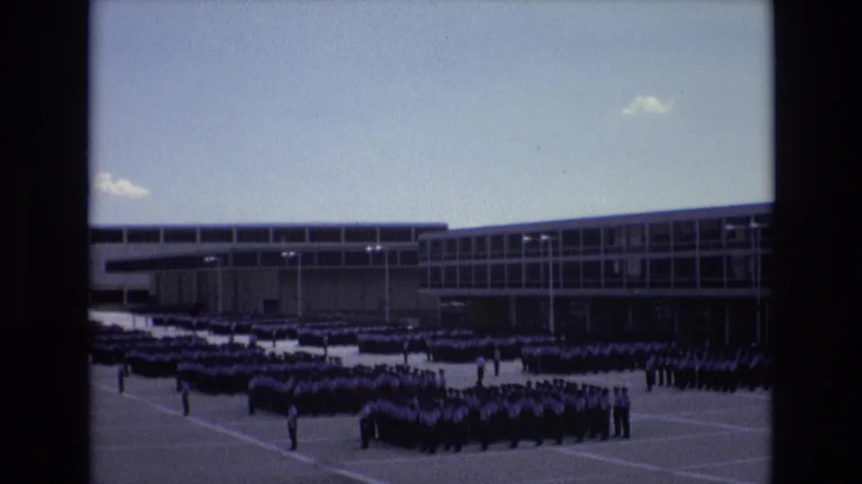 Distant 1973 Colorado Springs frame of uniformed men arranged in disciplined rows outside a long modern building under a clear sky.