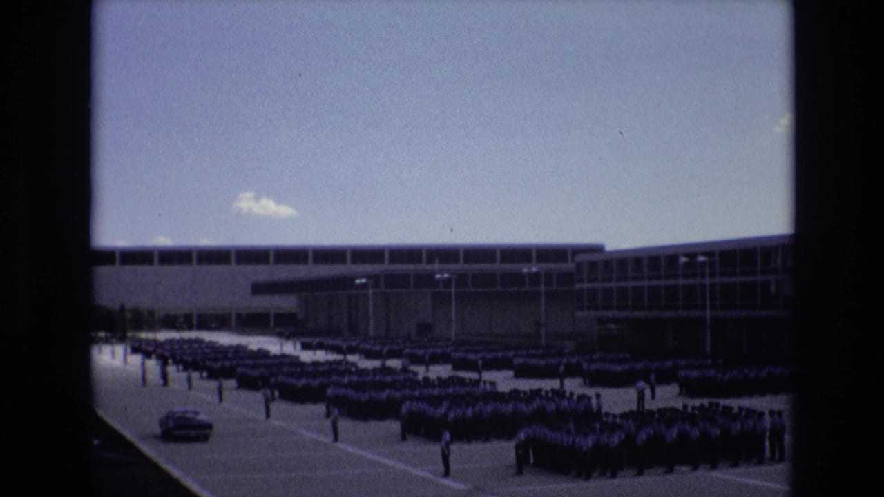 1973 Colorado Springs footage shows rows of cadets assembled in formation outside a modern institutional building, with a car visible at the left edge.