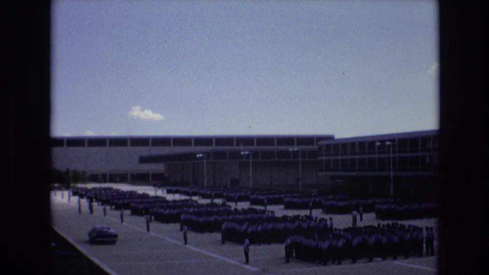 1973 Colorado Springs footage shows rows of cadets assembled in formation outside a modern institutional building, with a car visible at the left edge.