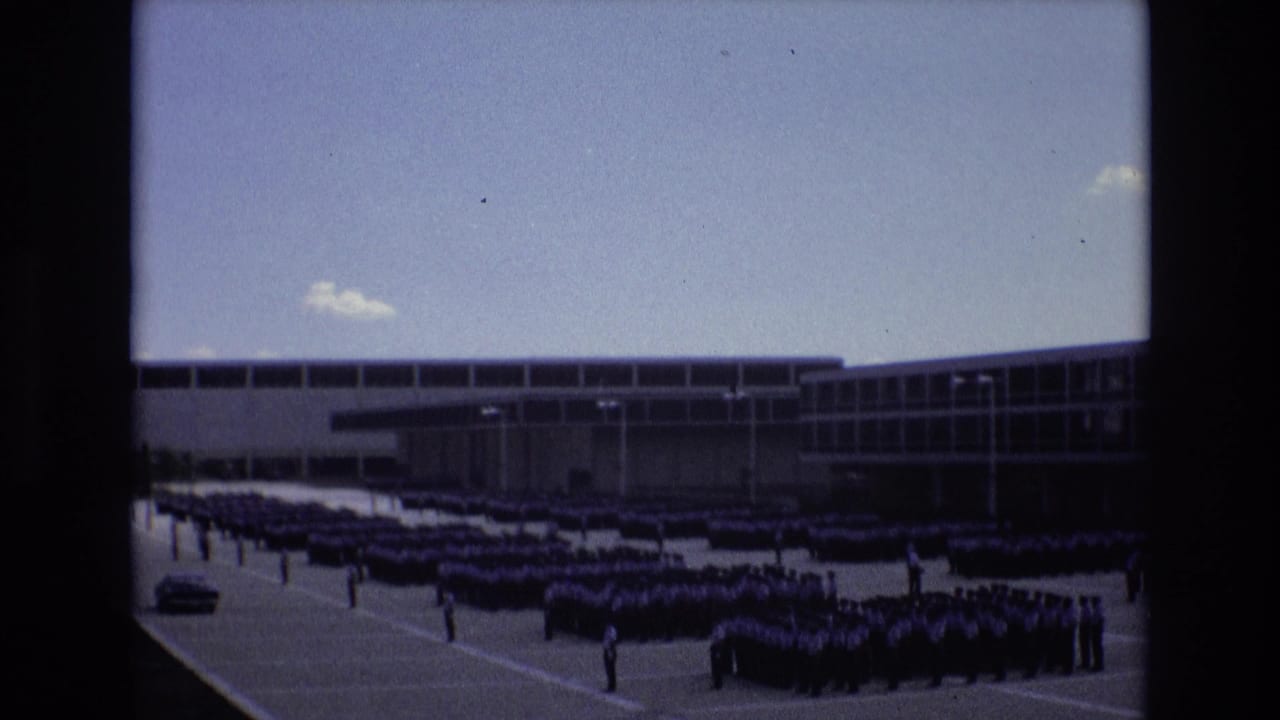 A wide view shows cadet ranks assembled in front of a large modern building.