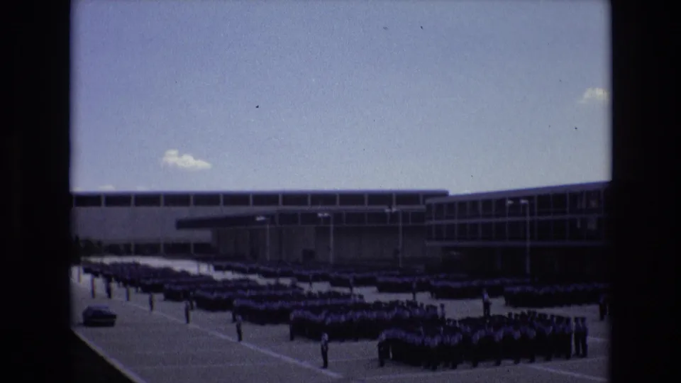 Wide 1973 Colorado Springs frame of uniformed cadets arranged in precise rows across a paved courtyard before a large institutional building.