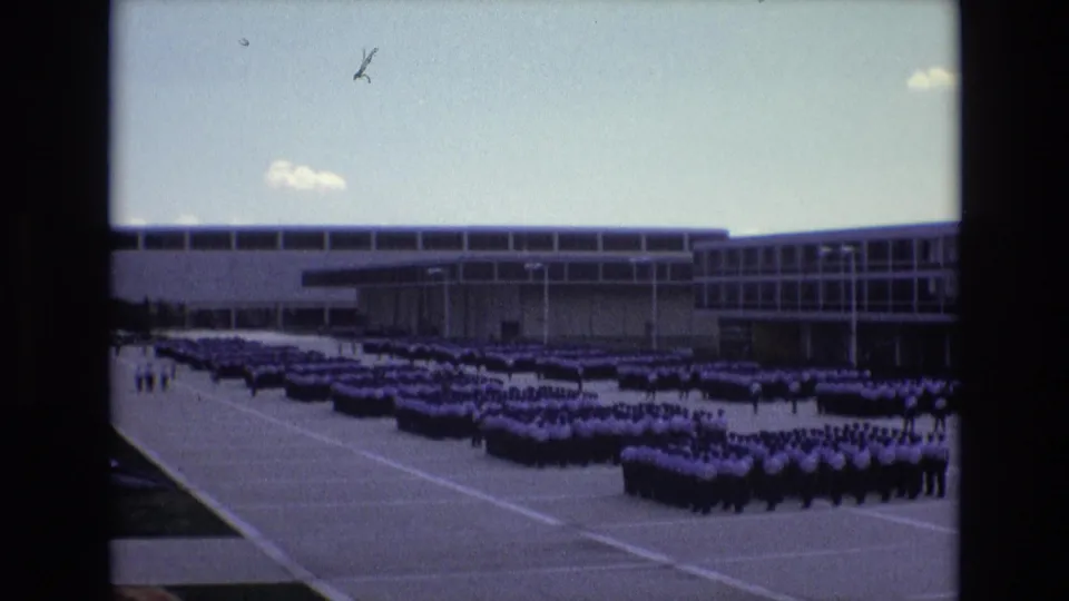 Final 1973 Colorado Springs frame shows distant cadet formations on a paved parade area, with the modern building and film dust marks visible.