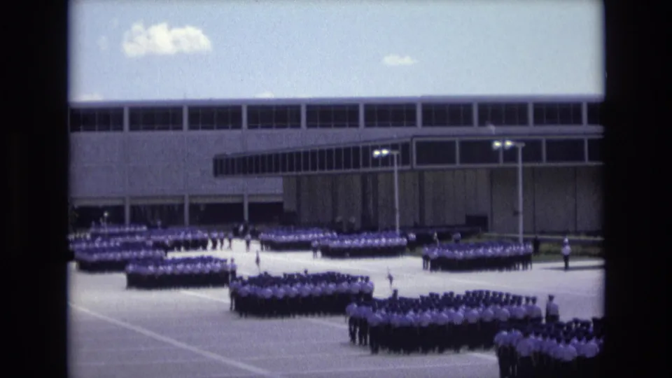 1973 Colorado Springs home-movie still with uniformed formations in the foreground and middle distance outside a large modernist building under daylight sky.