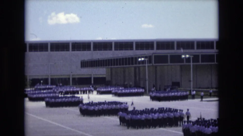 1973 Colorado Springs 8mm still showing uniformed ranks and small flags spread across a paved assembly space outside a large windowed structure.