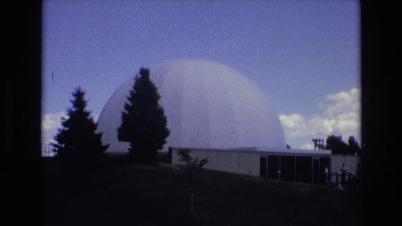 Large white dome with trees and a low building in front.