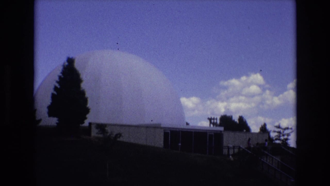 1973 Colorado Springs 8mm frame showing a large white dome rising behind a low building, with silhouetted trees and clouds in the sky.