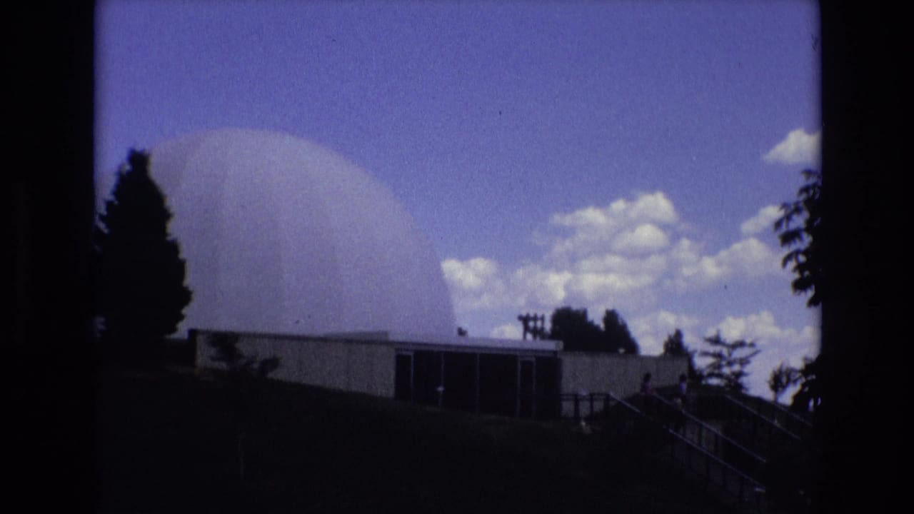 White dome and low building framed by dark trees and clouds.