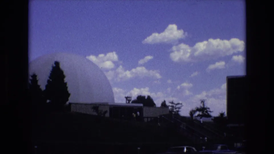 1973 Colorado Springs home-movie view of a white geodesic dome, stairway area, dark foreground trees, older cars, and small visitors near the entrance zone.