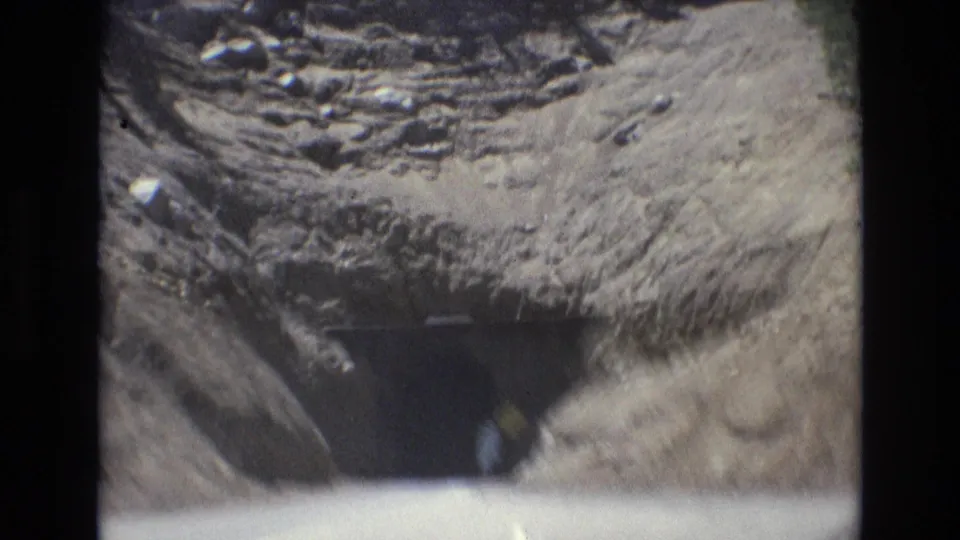 Soft 8mm frame from the 1973 Colorado Springs clip showing the road and rocky tunnel entrance from a moving vehicle perspective.