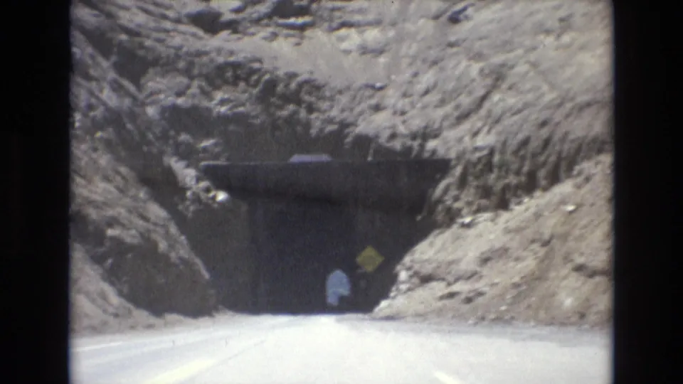 1973 8mm Colorado Springs road scene showing a close approach to a dark mountain tunnel with a yellow roadside sign beside the entrance.