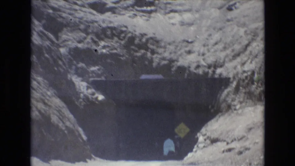 1973 Colorado Springs home-movie frame showing the vehicle nearing a shadowed tunnel cut into rock, with a yellow clearance sign visible near the entrance.