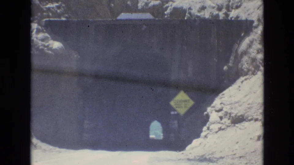 1973 Colorado Springs 8mm frame showing the car close to the tunnel mouth, with the yellow clearance sign more prominent against the dark entrance and rocky hillside.