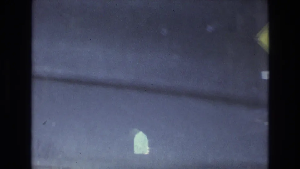 A shadowed 8mm frame from inside the tunnel shows the passage in low light, a partially visible yellow sign, and small bright shapes ahead.