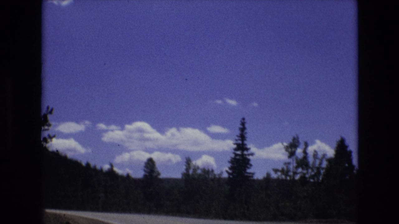 1973 8mm Colorado travel footage shows a winding road along forested hills beneath a blue sky with scattered white clouds.