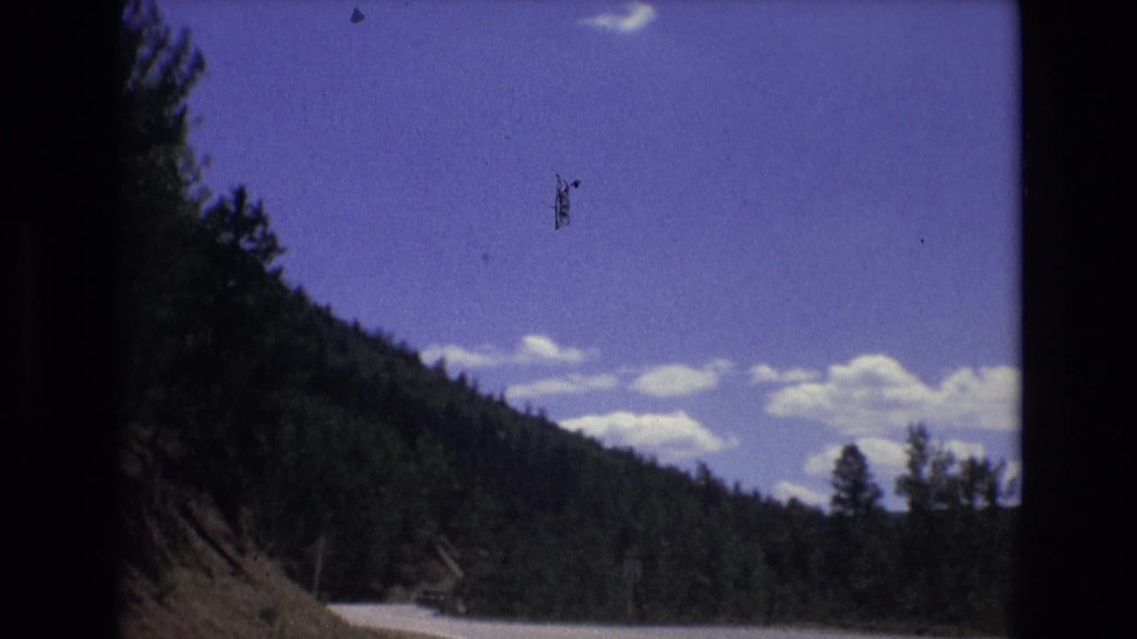 1973 Colorado Springs-area 8mm footage appears to show a road running below a wooded mountain slope with clouds across a blue sky.