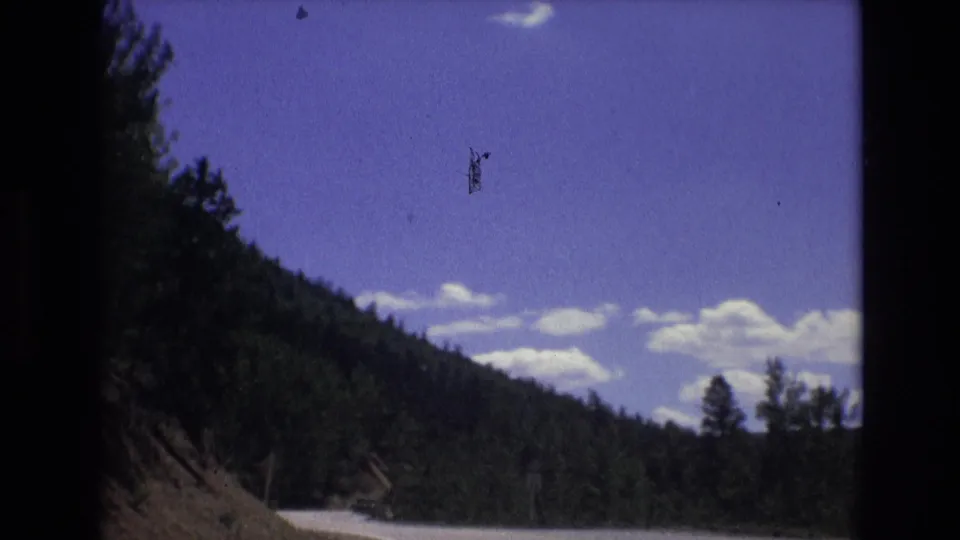 1973 Colorado Springs-area 8mm footage appears to show a road running below a wooded mountain slope with clouds across a blue sky.