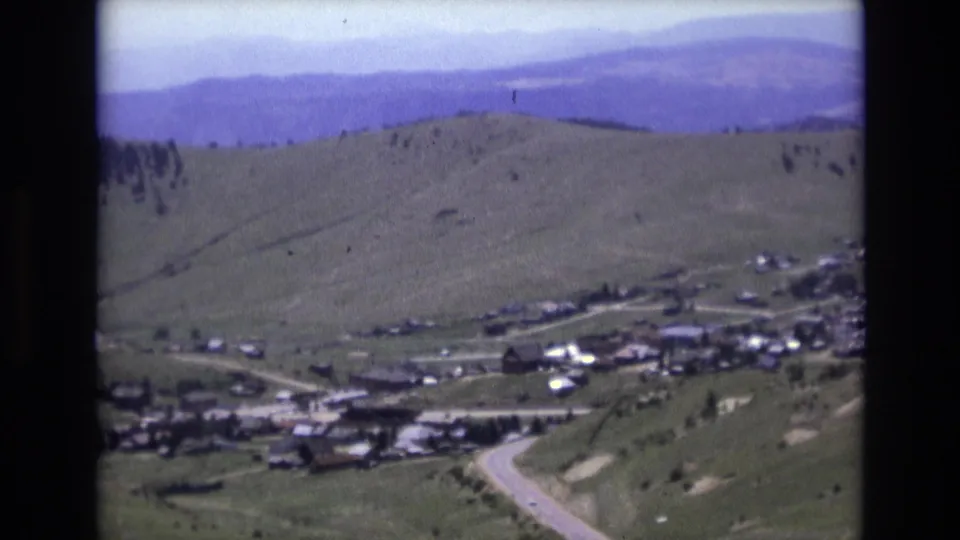 1973 Colorado Springs-area home-movie footage shows roads and buildings in a valley with open green hills and distant mountain ridges.