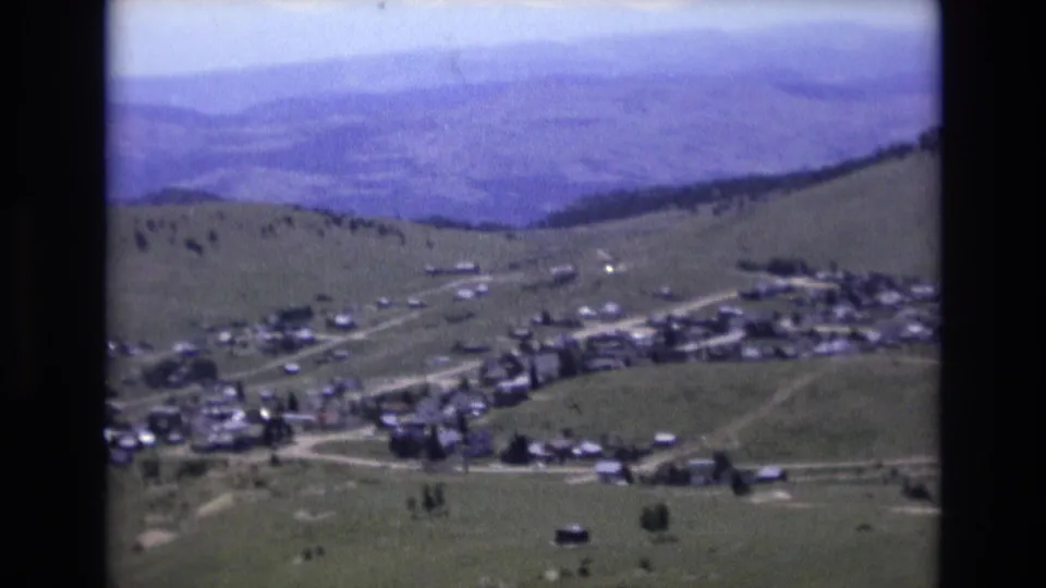 1973 8mm frame showing a Colorado Springs-area valley town from above, with curving roads, scattered structures, open slopes, and hazy mountain layers.