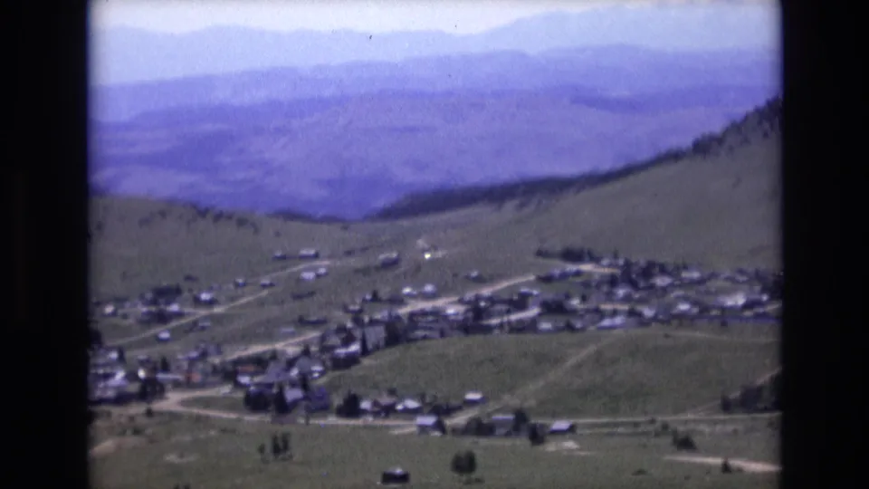Final 1973 home-movie frame looking across a Colorado Springs-area hillside settlement, open valley ground, pale roads, and soft blue mountain ridges.