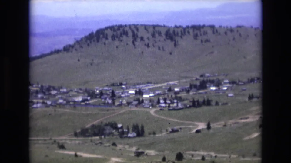 Late-frame 1973 8mm view near Colorado Springs with roads, small buildings, open fields, a tree-dotted foothill, and muted blue mountain haze.