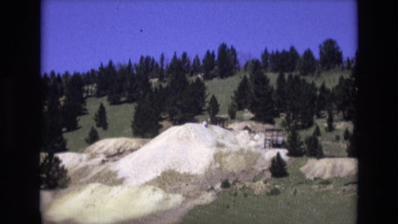 1973 Colorado Springs 8mm frame showing a pale white and yellowish rock face below a pine-covered hillside under a saturated blue sky.