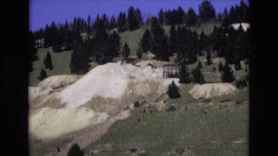 Colorado Springs 8mm frame showing a pale rock face, grassy slope, scattered pines, and a small fence-like or wooden structure near the formation.
