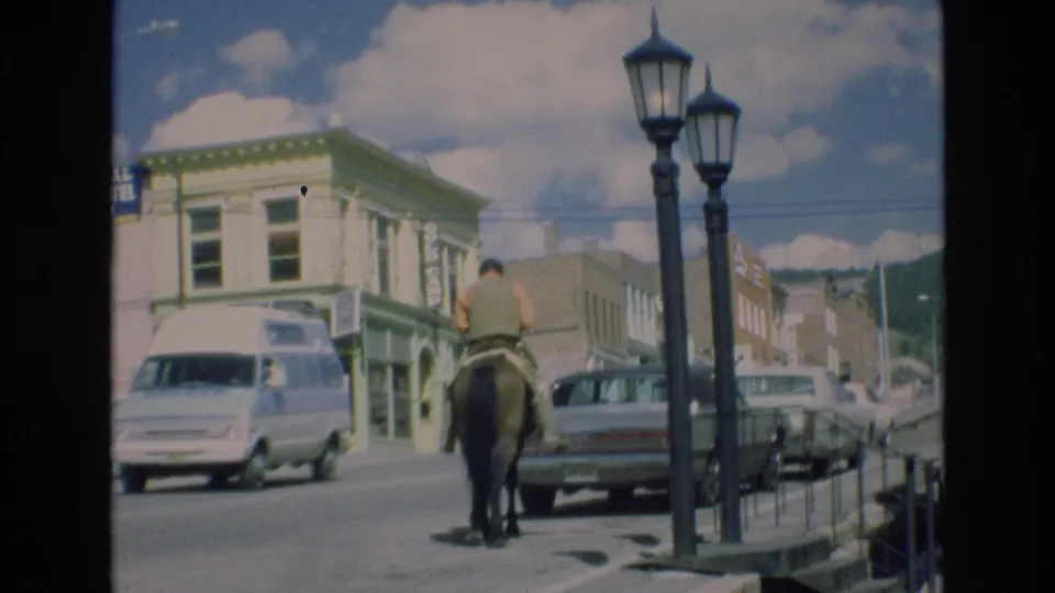 At the end of the clip, the rider moves away on horseback through the 1973 Colorado Springs street scene, with classic vehicles, storefronts, railings, and streetlamps still visible.