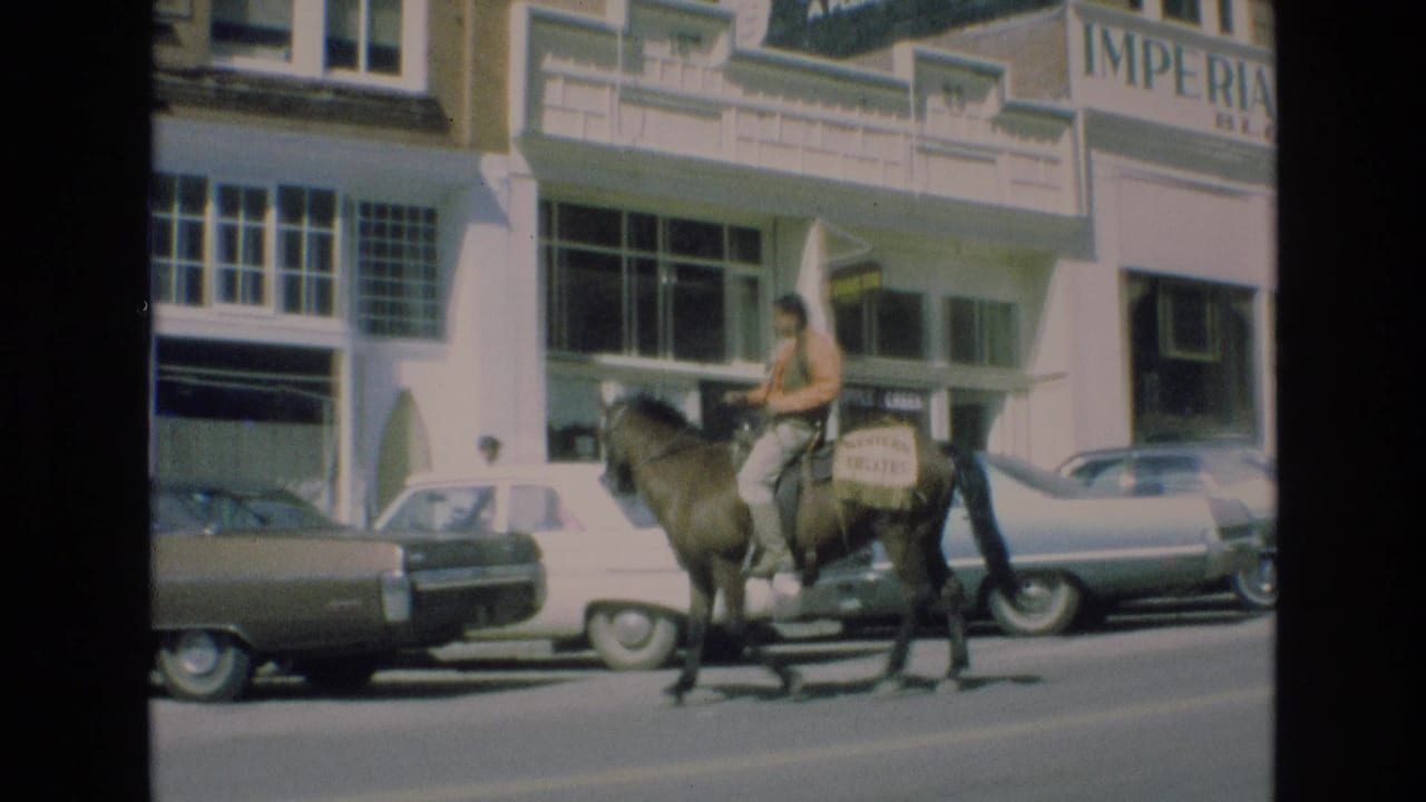 A sleeveless rider on horseback passes parked cars and commercial storefronts in downtown Colorado Springs, with hotel-block signage partly visible above the sidewalk.
