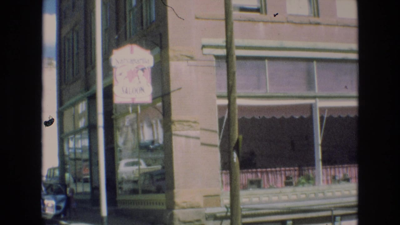 Brick storefront and saloon sign seen across a street with a utility pole in front.