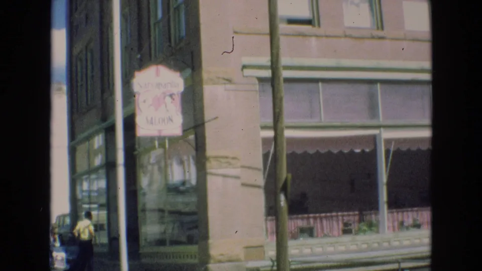 1973 Colorado Springs street-corner view showing the Saraparilla Saloon sign, storefront windows, utility pole, and a small distant pedestrian near parked cars.