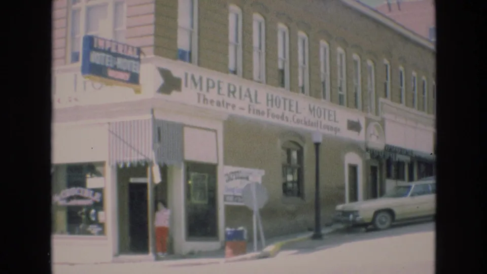 Wider 1973 Colorado Springs street view of the Imperial Hotel-Motel building, showing its long facade, prominent commercial signage, entrance area, sidewalk sign, pedestrian, and parked sedan.