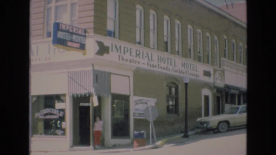 1973 Colorado Springs frame centered on the Imperial Hotel-Motel sign and corner entrance, with striped awnings, a sidewalk sign, a pedestrian near the doorway, upper-floor windows, and a parked car at the curb.