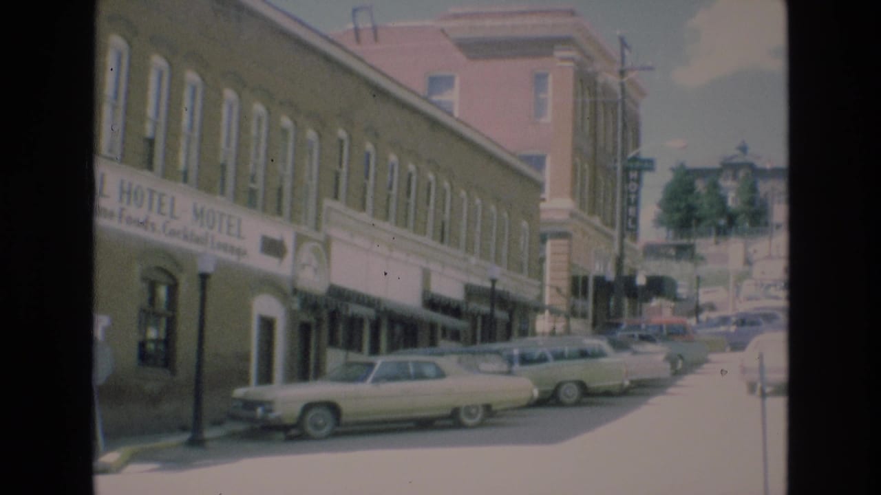 Long hotel-motel facade with classic cars parked along the curb and buildings up the street.