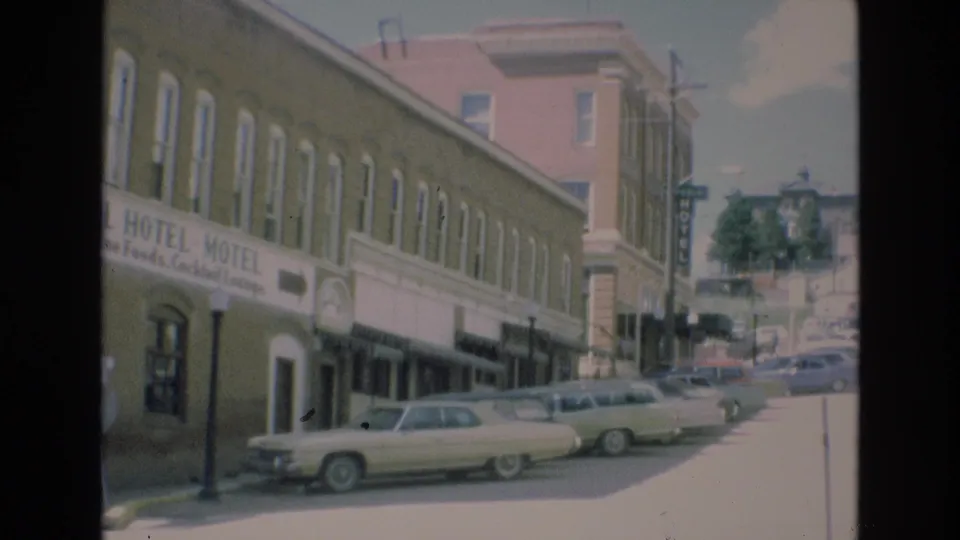 Colorado Springs 1973 home-movie frame showing the Imperial Hotel-Motel side of the street, classic automobiles, storefront awnings, and the road extending past the block.