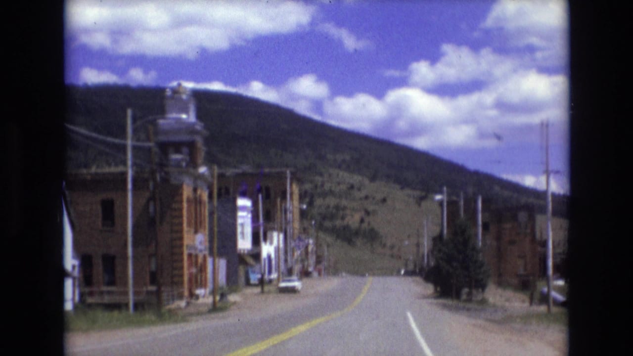 Curving road through a small town with storefronts and hillside in the background.