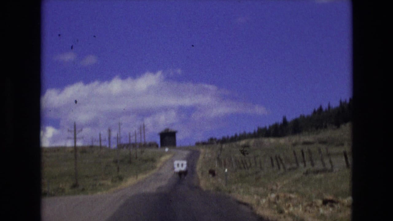 Rural paved road climbing through open fields toward a small dark structure.