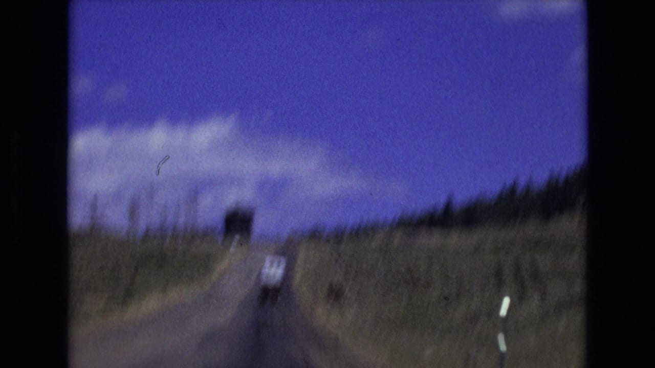 Blurred white van ahead on a rural road with fence posts and open hills.