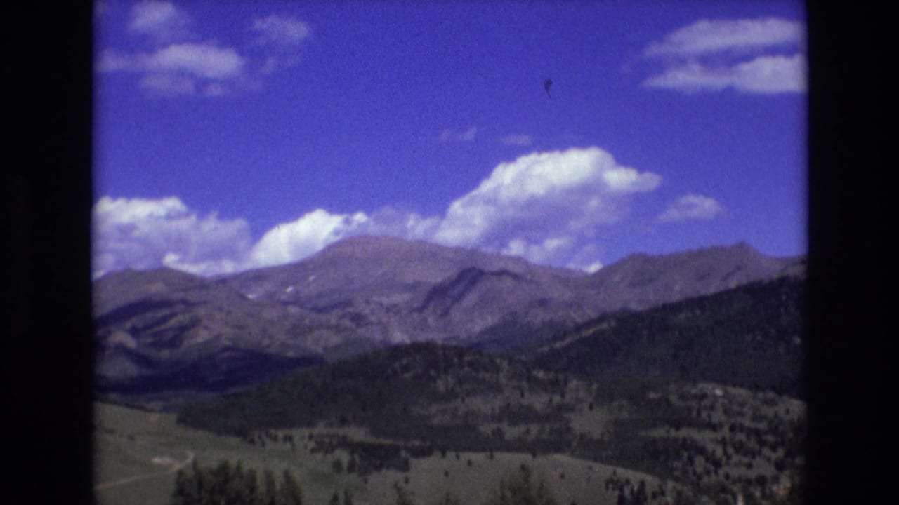 Mountain ridges and forested foothills beneath a bright blue sky with scattered clouds.