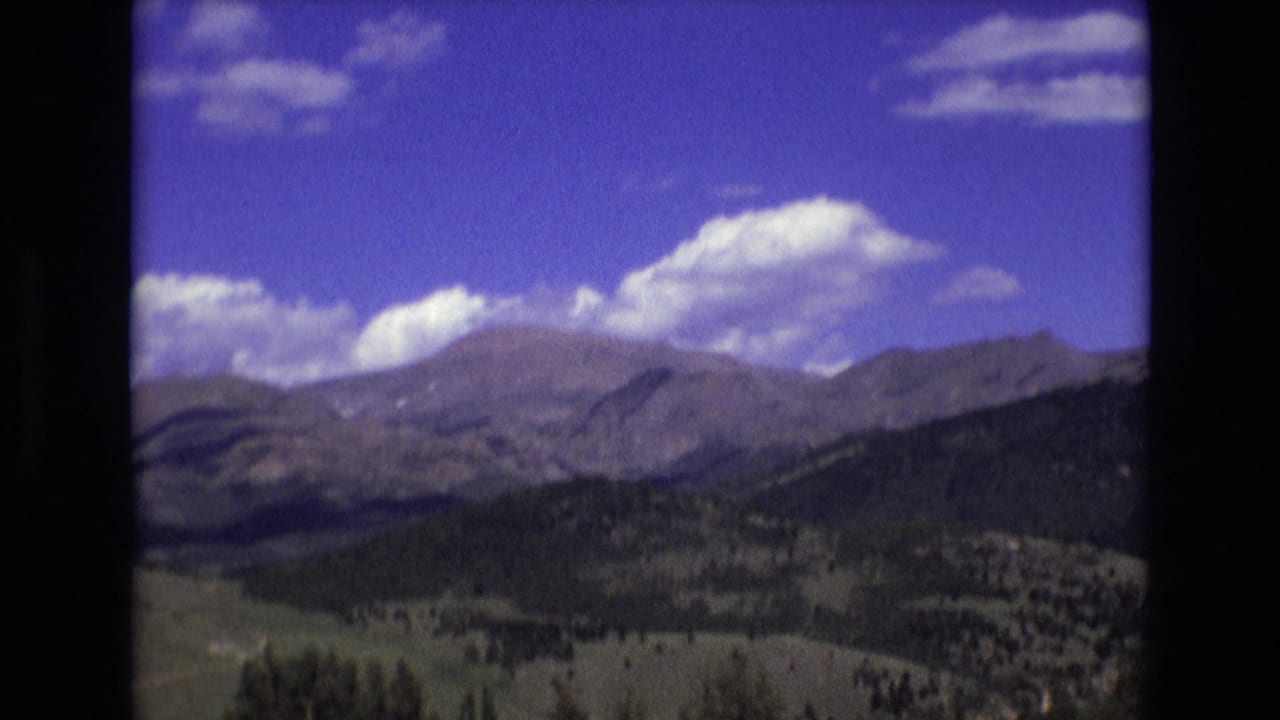 Distant mountain range under blue sky with clouds and forested foothills.