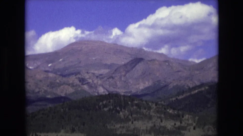 1973 8mm home-movie frame from Colorado Springs showing a broad mountain ridge, dark foothills, and white clouds against a saturated blue sky.