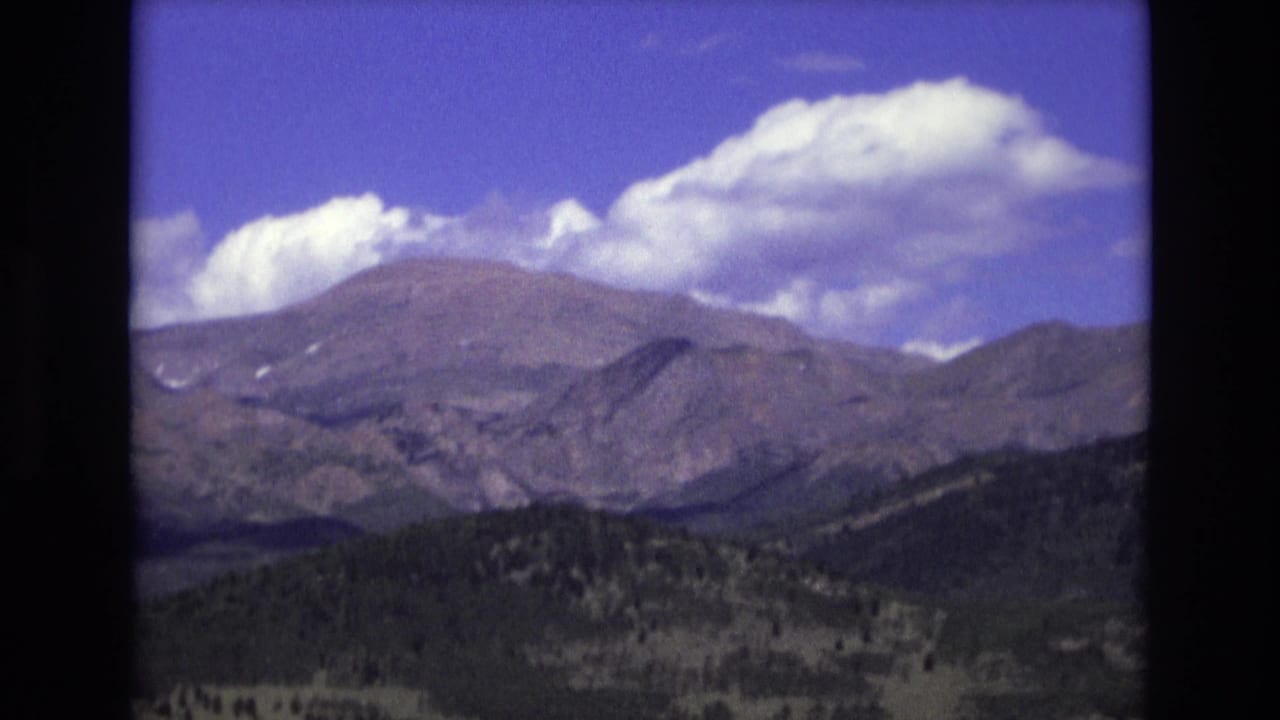 Rocky mountain slopes and dark foothills beneath large white clouds.