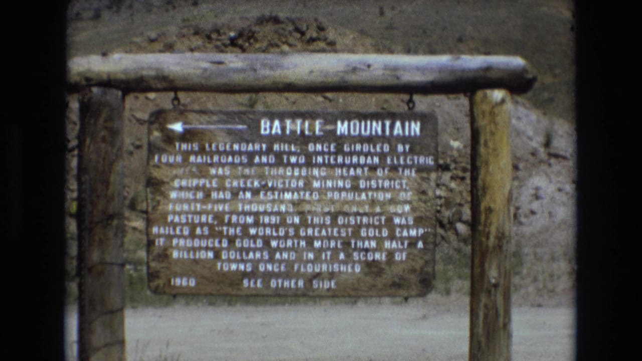 Battle Mountain historical marker in Colorado, filmed close enough to show the title and mining-history text, with rough timber supports and dry hillside behind it.
