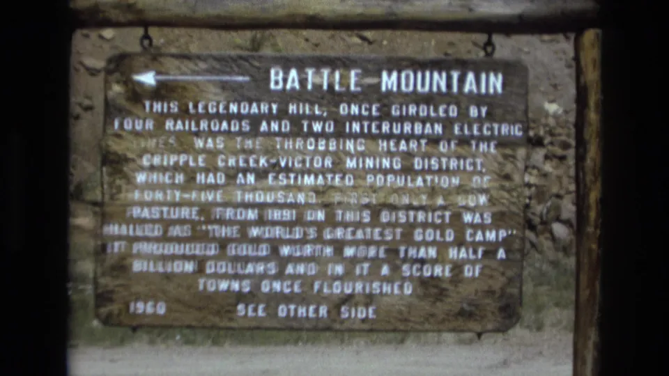 Close 8mm frame of the Battle Mountain historical marker, emphasizing the sign title, weathered board, and text about the Cripple Creek-Victor mining district.