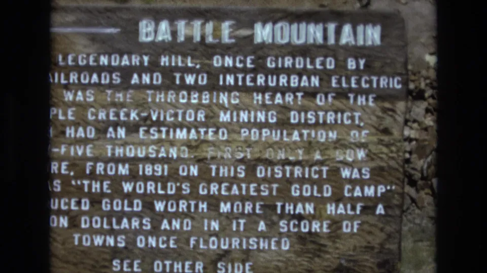 1970s 8mm home-movie frame with the camera closer on the Battle Mountain marker, showing enlarged white lettering and the phrase See Other Side near the bottom.